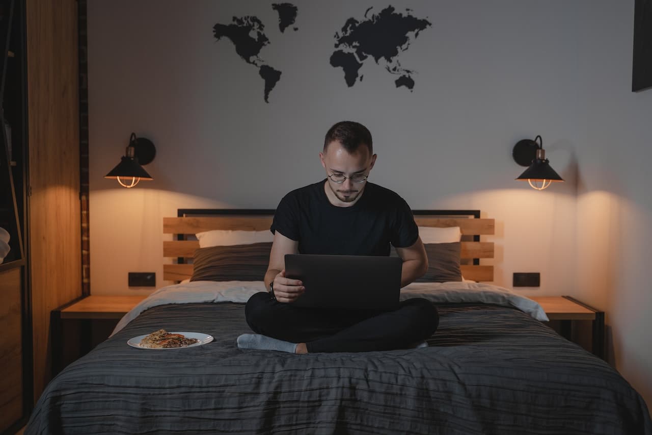 a man using a laptop while sitting on bed