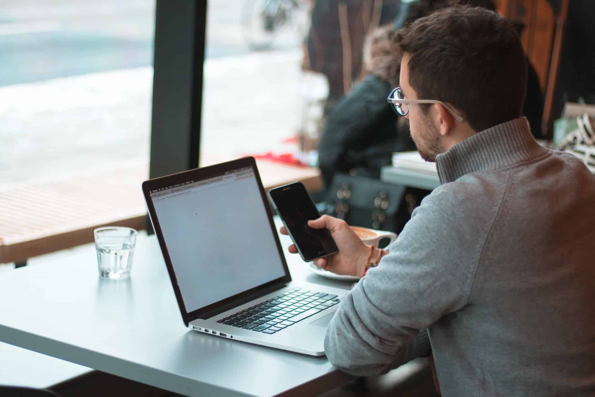 man sitting at table with laptop and cell phone