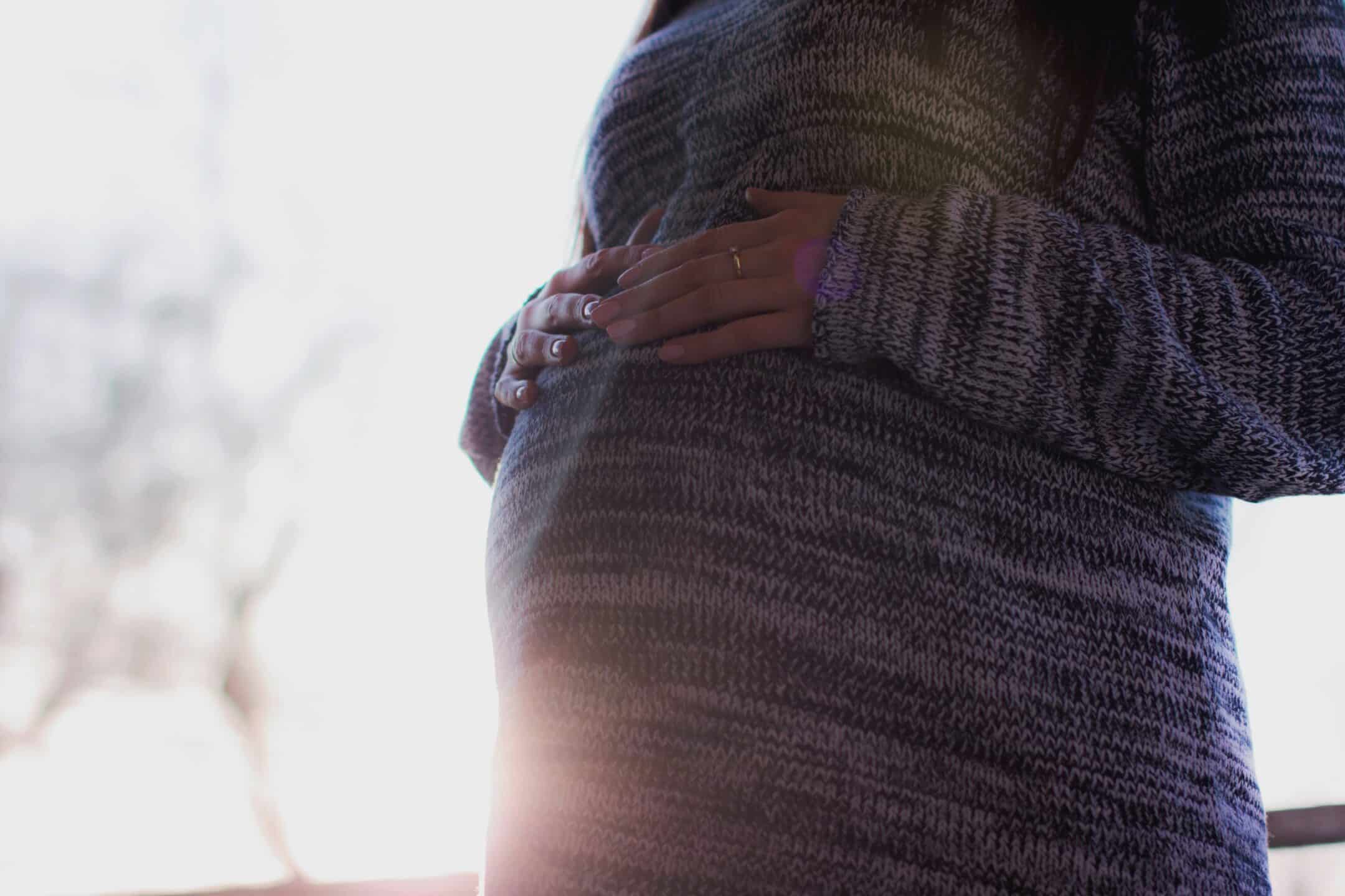 A pregnant woman with the sun behind her and her hands resting on her belly, representing pregnancy discrimination.