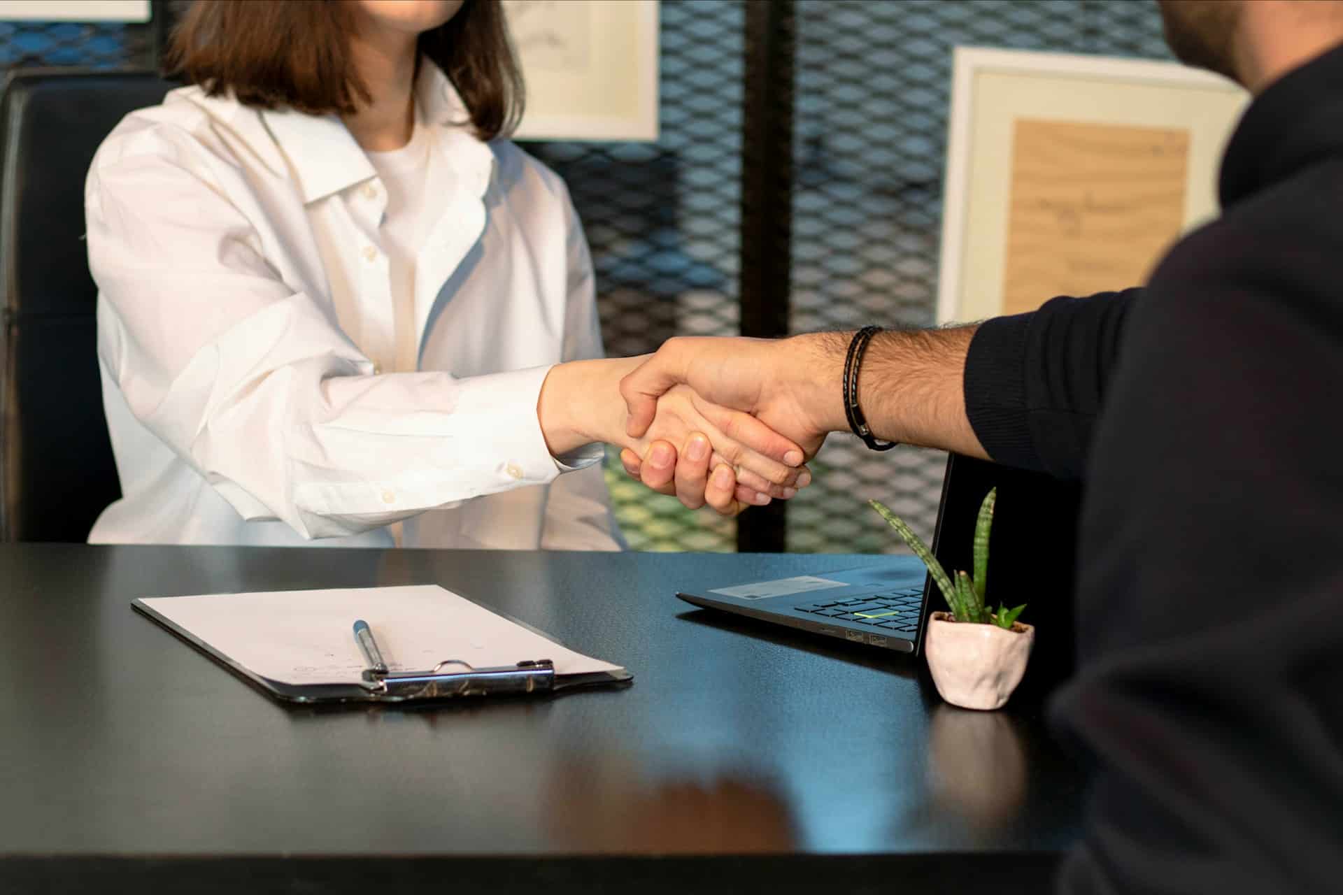 A man and woman shaking hands over a desk, representing reference check laws.