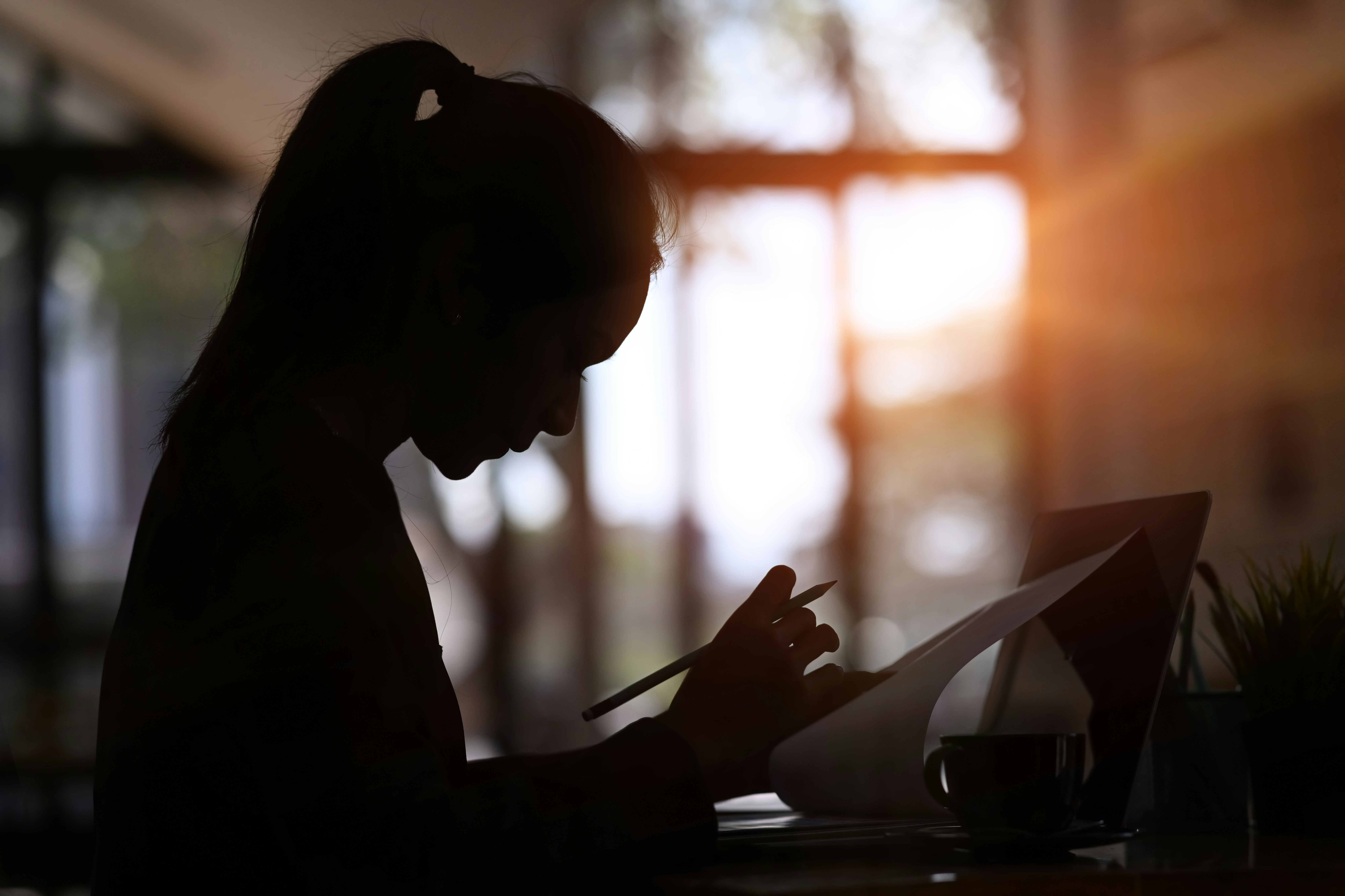 A silhouette of a woman writing a document at her desk, representing anonymous employee complaints and workplace investigations in Ontario.
