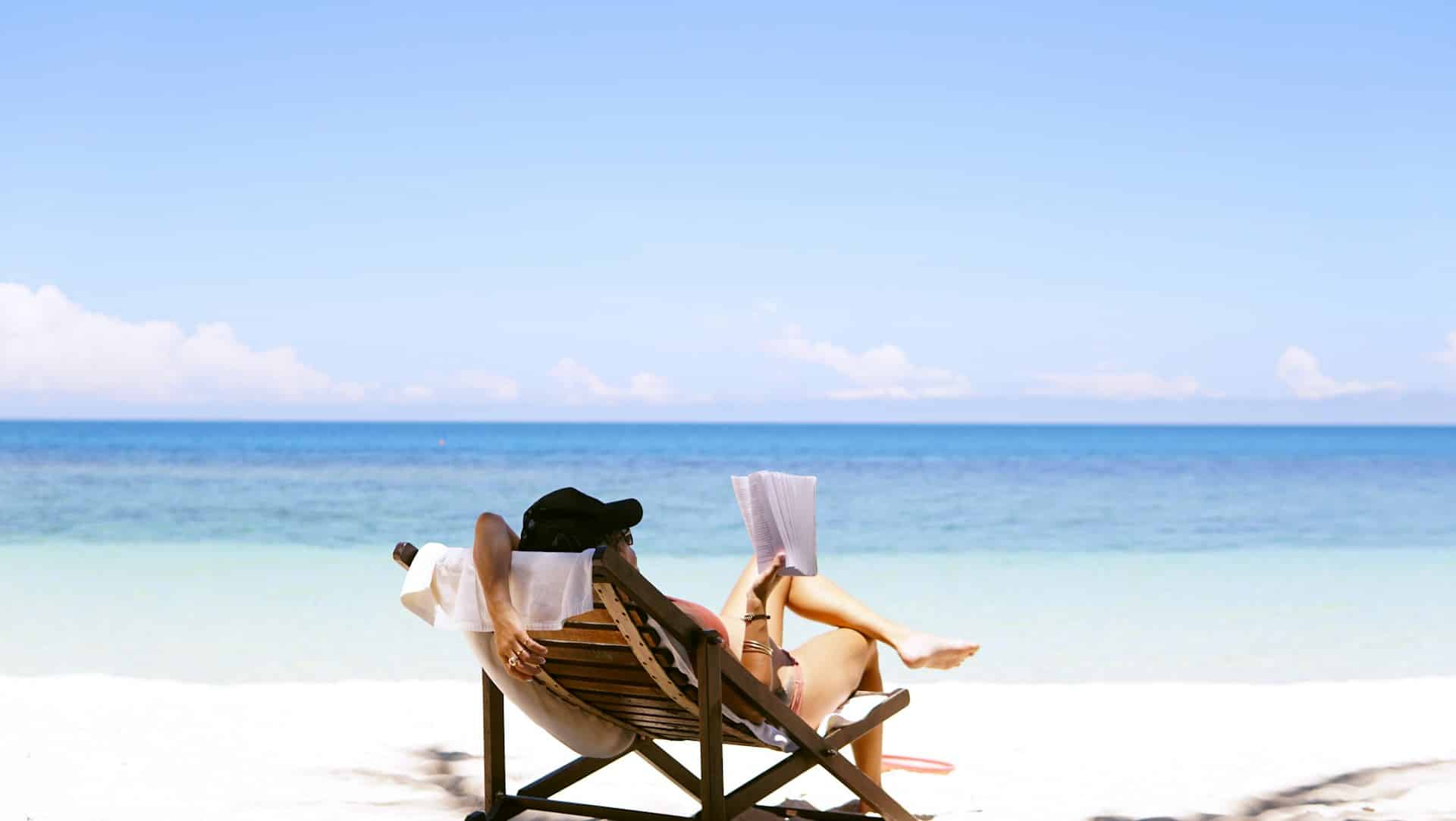 A person relaxes in a beach chair, reading a book by the clear blue ocean, symbolizing the importance of vacation time and understanding Ontario vacation rights employer policies.