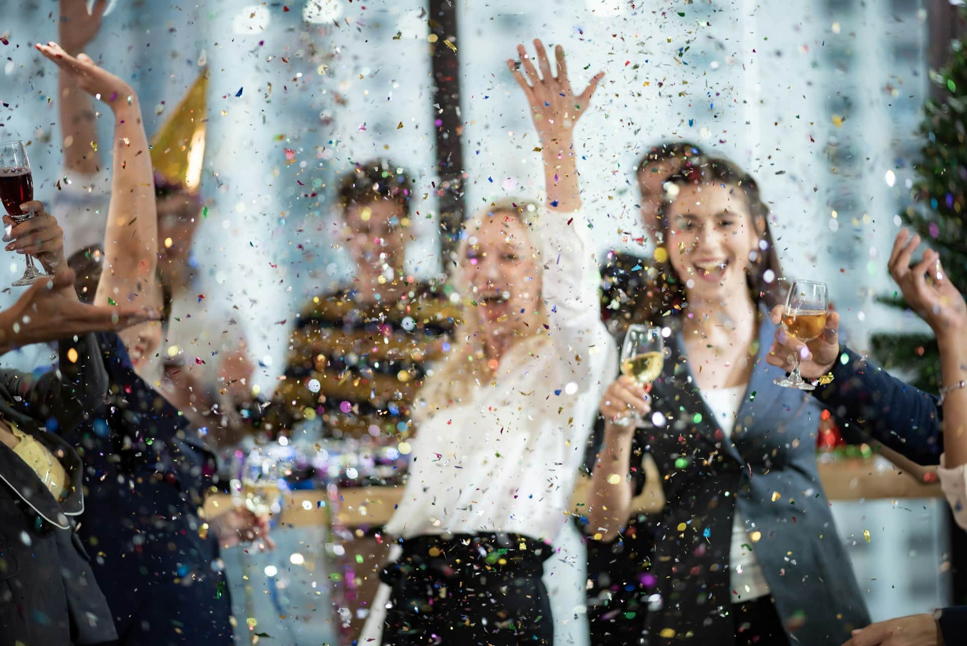 A group of employees celebrate at a holiday party in their office, enjoying glasses of wine while shimmering confetti falls around them, representing holiday party liability.