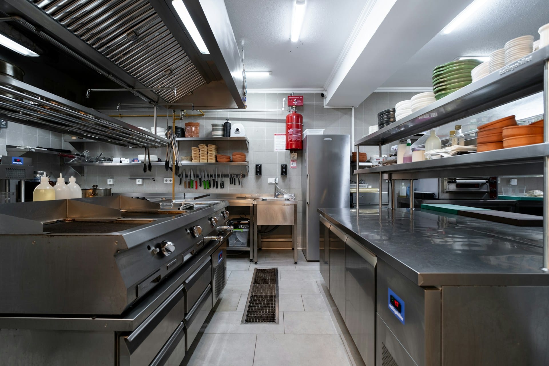 A commercial kitchen with a row of stainless steel ovens and stovetops on one side and countertops with shelves stacked with dishes, like the type of kitchen the plaintiff worked in, representing employment vs. labour law mistakes.