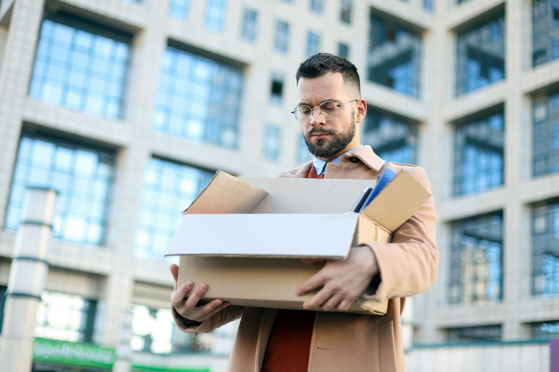 A man walks away from an office building while carrying his work belongings in a cardboard box, representing shareholder-employee terminations.