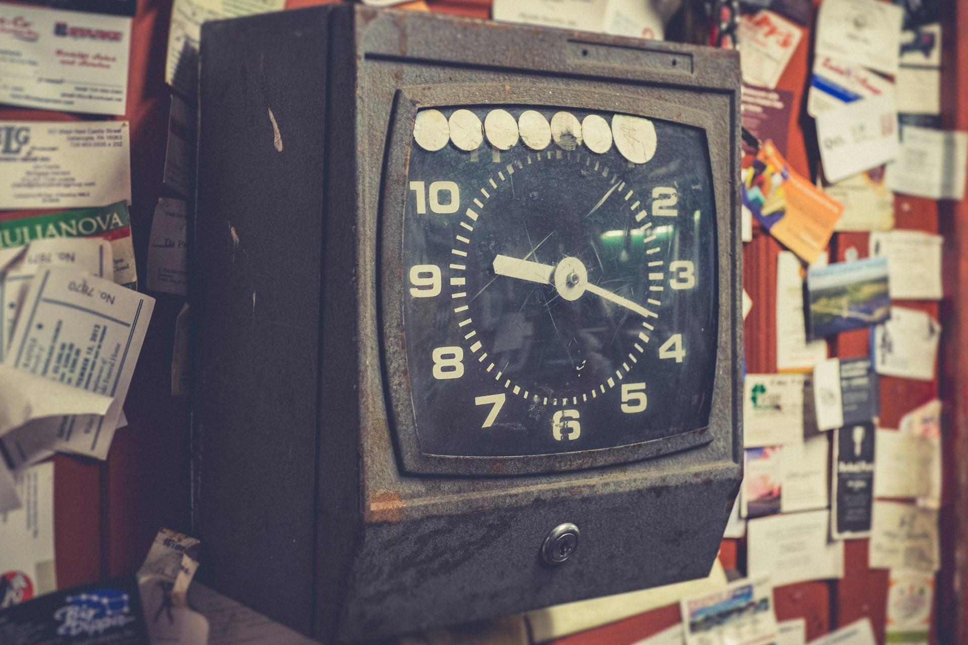 A punch clock is mounted on a wall and surrounded by pinned bulletins, representing time theft and just cause.