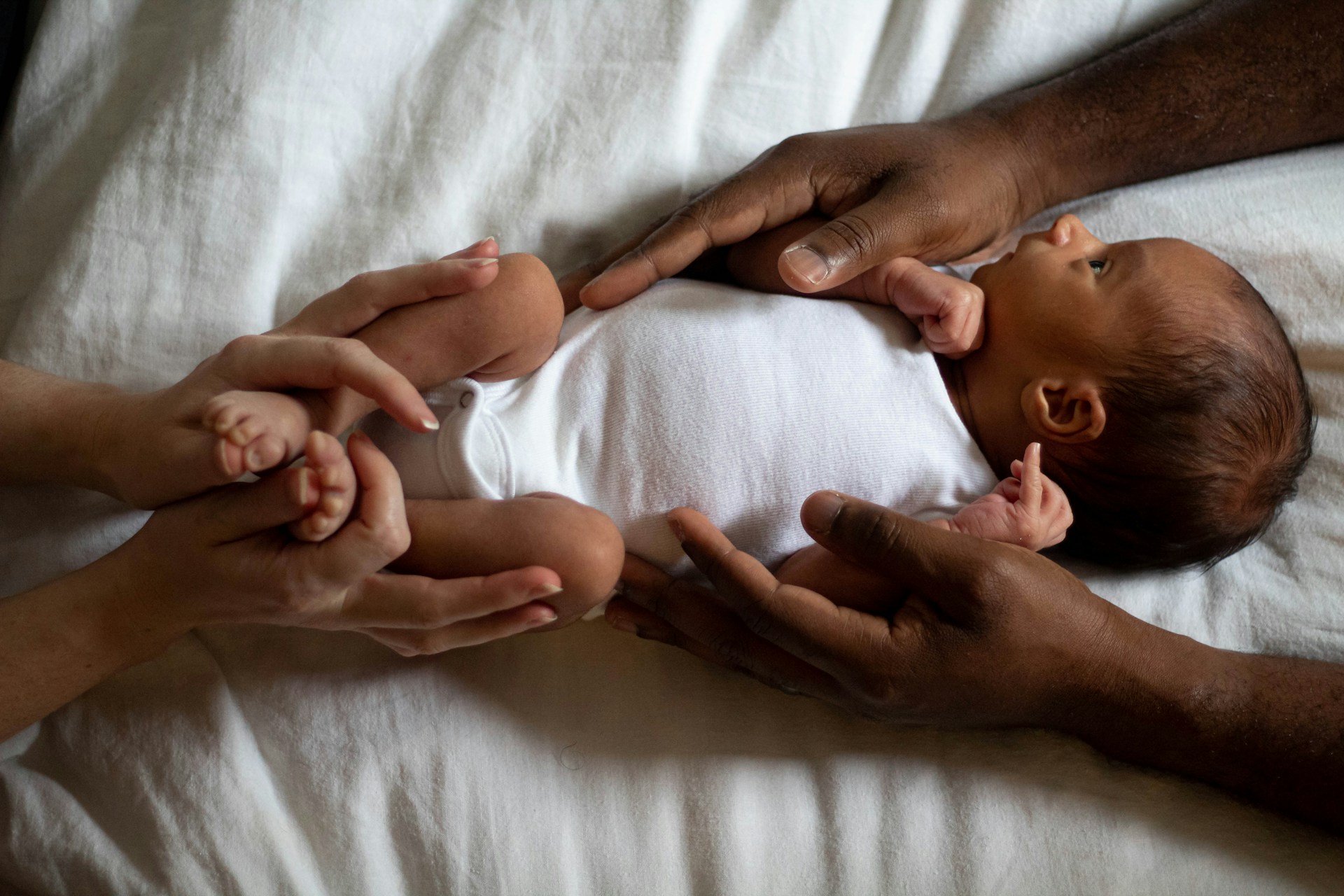 A man and a woman holding a new born baby while it lays on the bed, representing adoption and surrogacy leave.