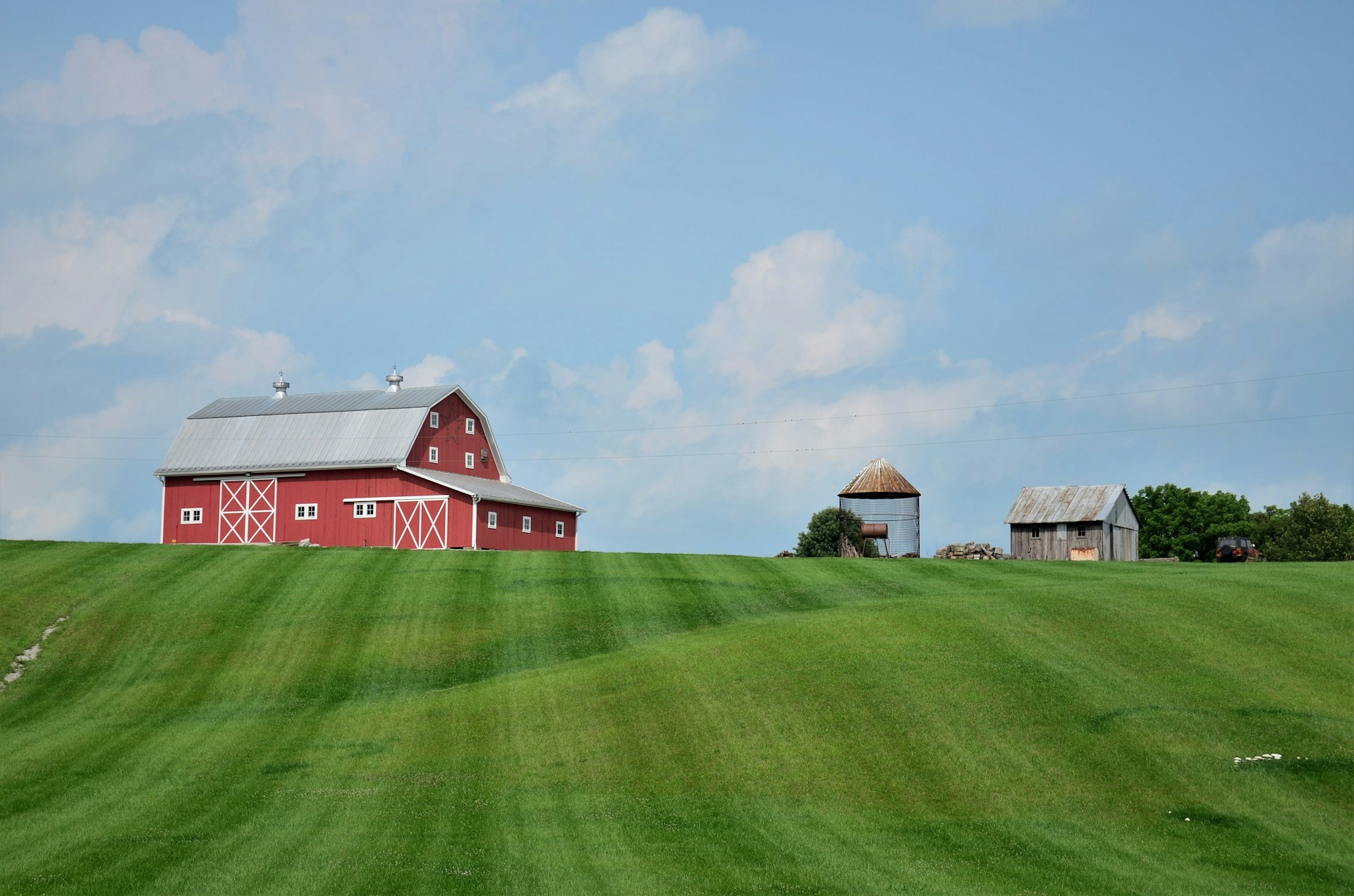 A red barn with white trim perched on a grassy hill with a short silo and a weathered shed next to it, representing dependent contractor constructive dismissal.