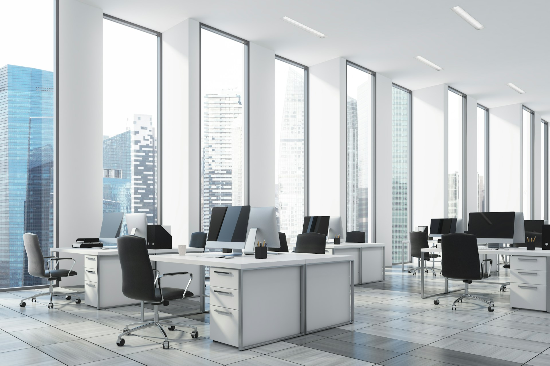 Rows of empty white desks with computers and black chairs and tall windows lining one white wall looking out onto the city, representing condonation and just cause.