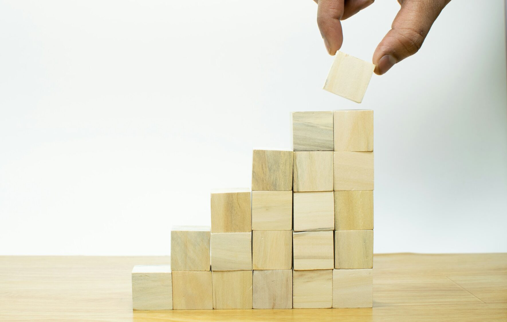 A hand placing a block on top of a stack of wooden building blocks, representing corporate restructuring and constructive dismissal risks in Ontario employment law.